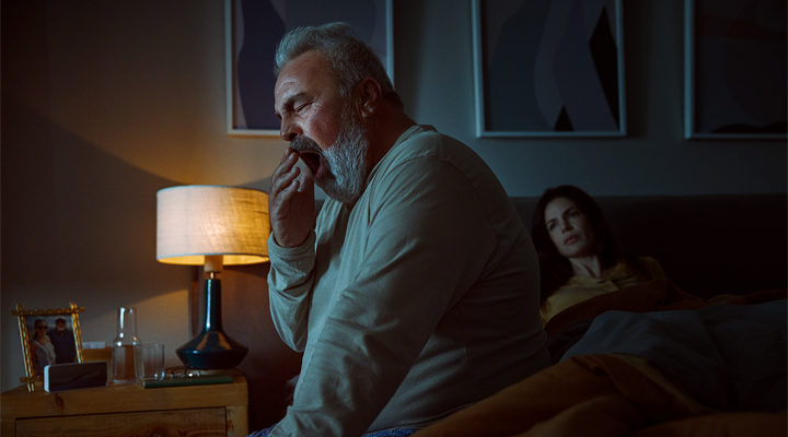 Man sitting in the bed yawning.